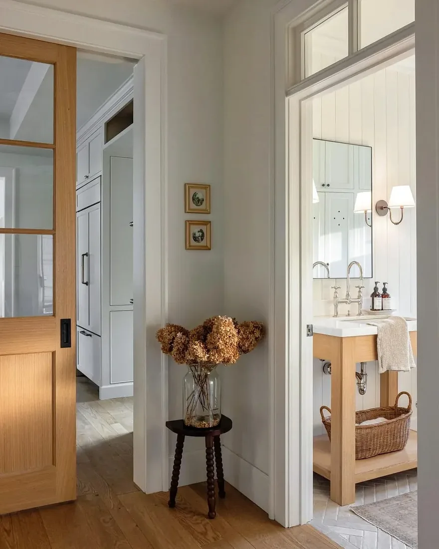 Light oak open vanity with white basin seen through a doorway beside white panelling