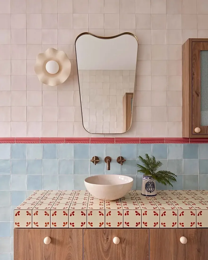 Bathroom with pink tile above a red pencil trim, blue zellige below and a patterned tiled vanity top