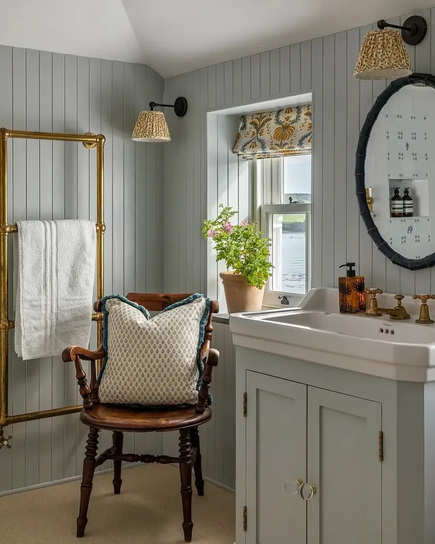 Pale blue panelled bathroom with white vanity, brass rail and timber chair