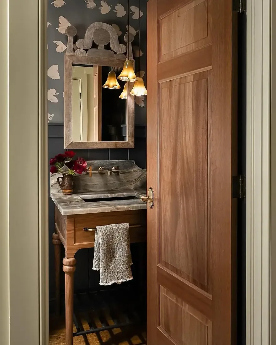 Small dark powder room seen through an oak door with marble vanity top and butterfly wallpaper