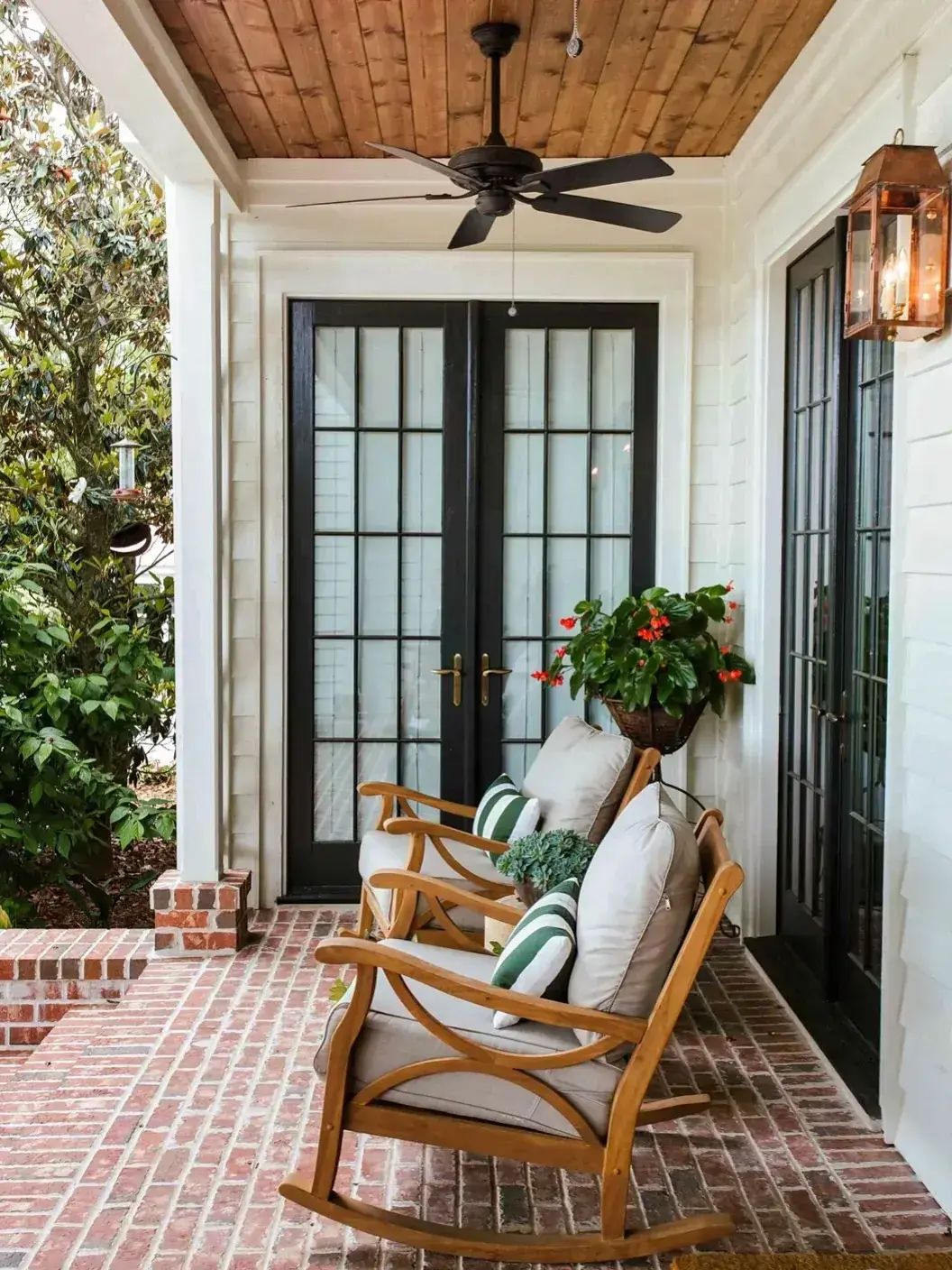 Black glazed double doors with brass handles on a brick porch with rocking chairs