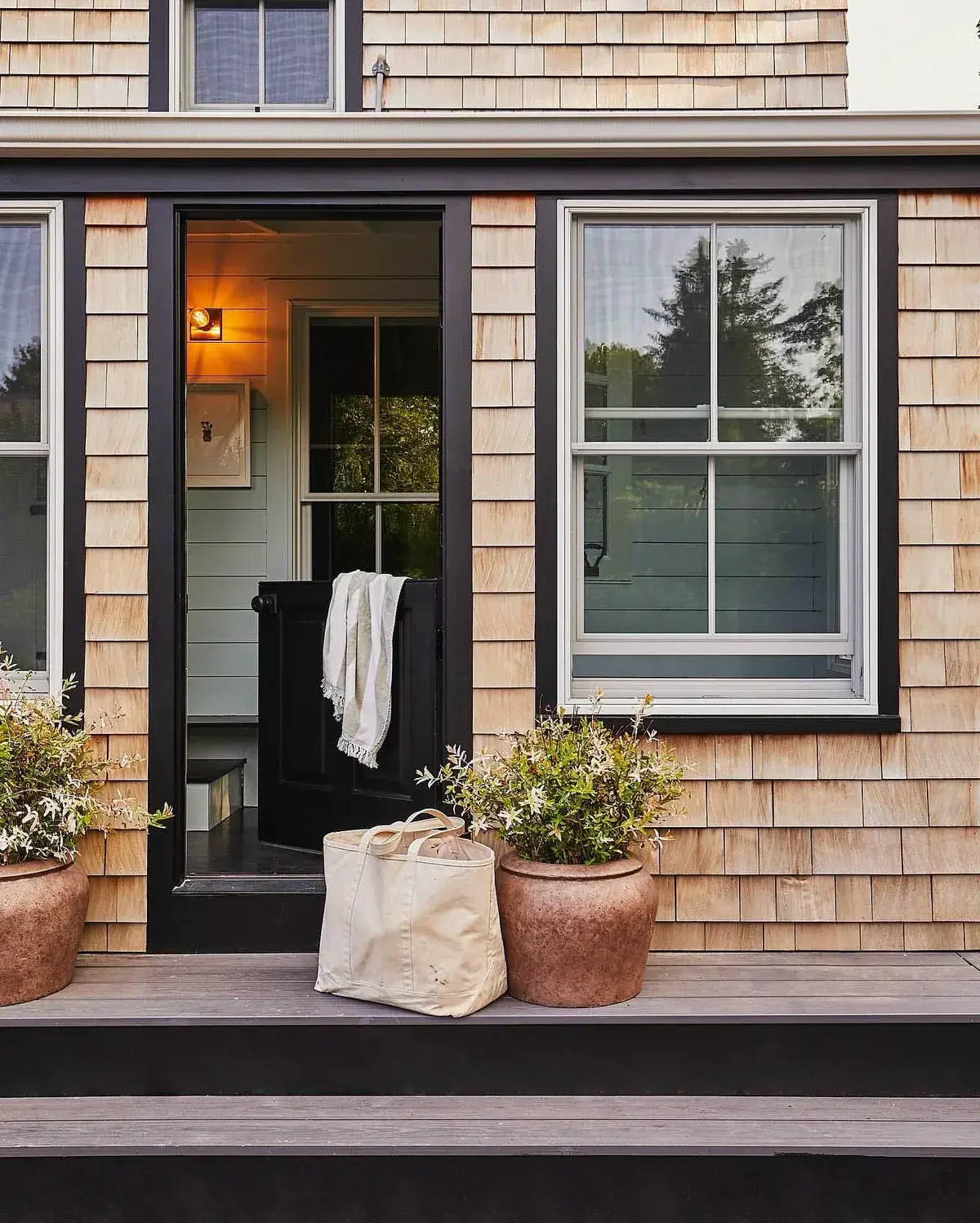Cedar shingle porch with black trim framing a half open black door and terracotta pots