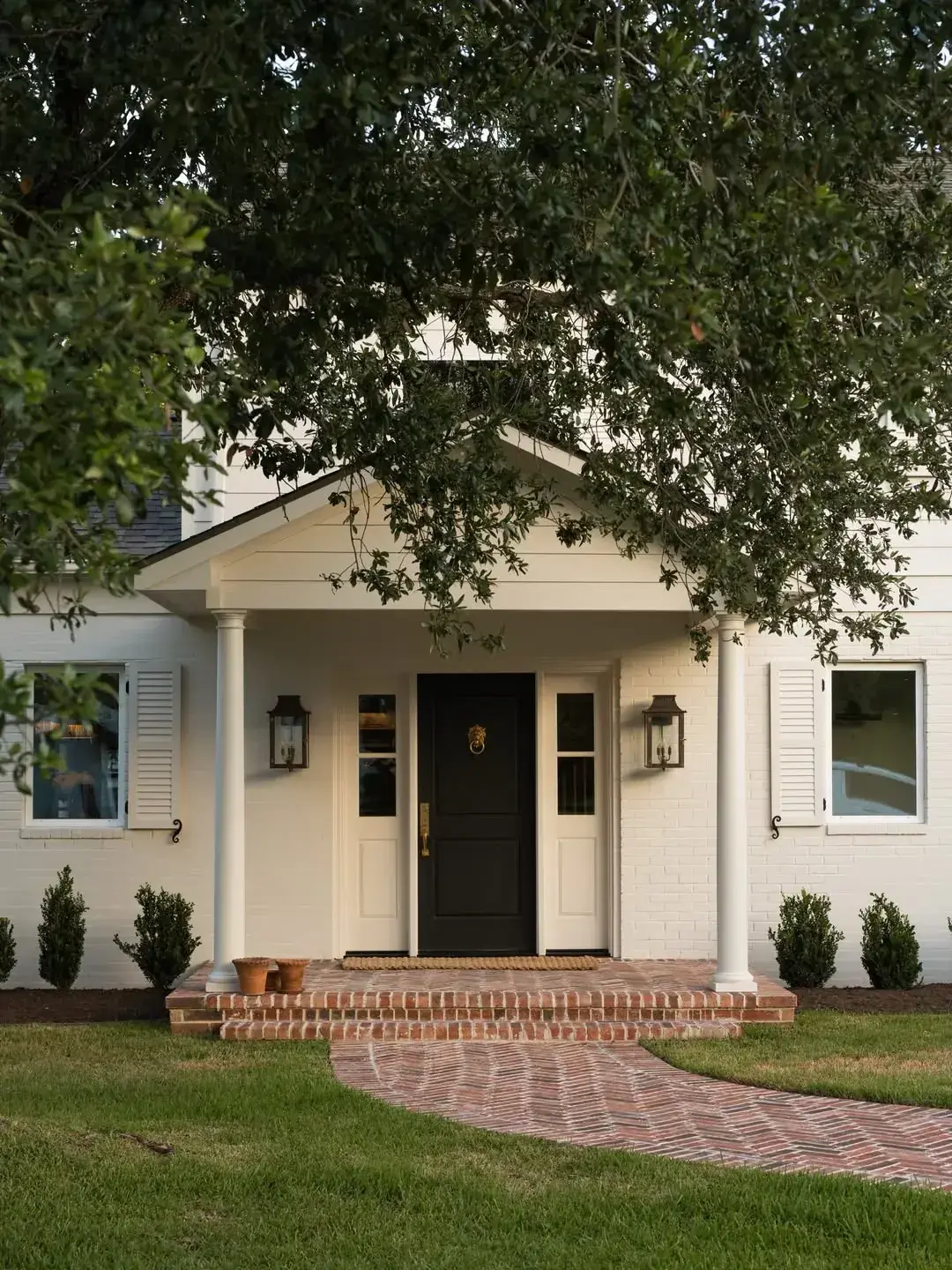 Cream brick house with a black panelled door between white sidelights and twin lanterns
