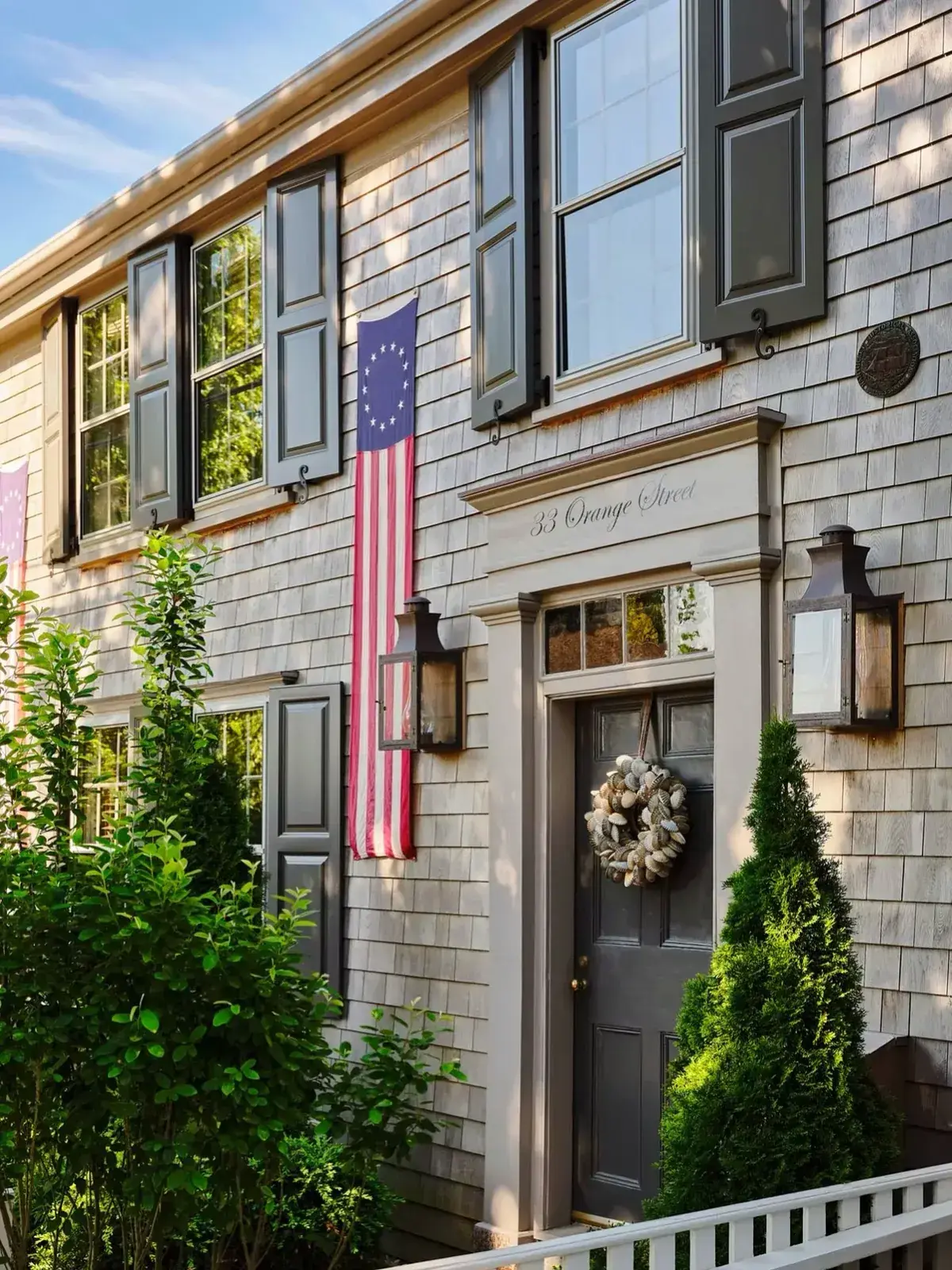Grey shingle townhouse with a dark panelled door, grey shutters and an oyster shell wreath