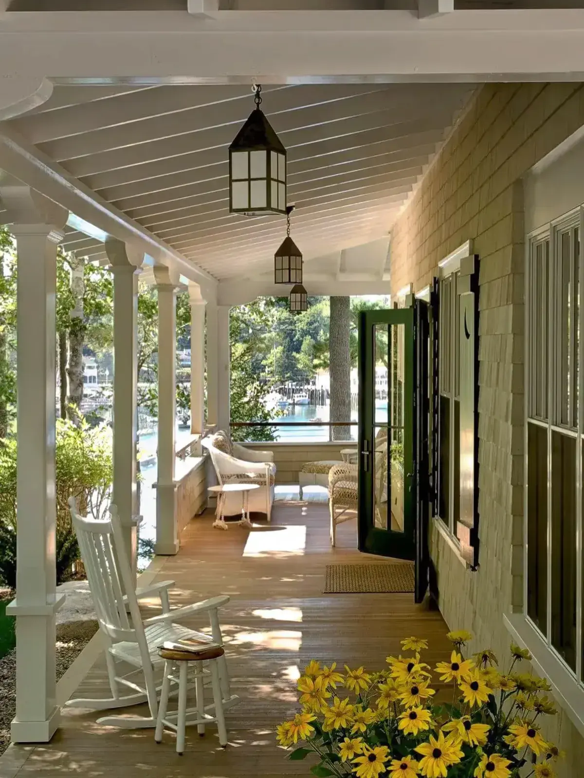 Long shingle porch with an open dark green glazed door, black pendant lanterns and yellow flowers