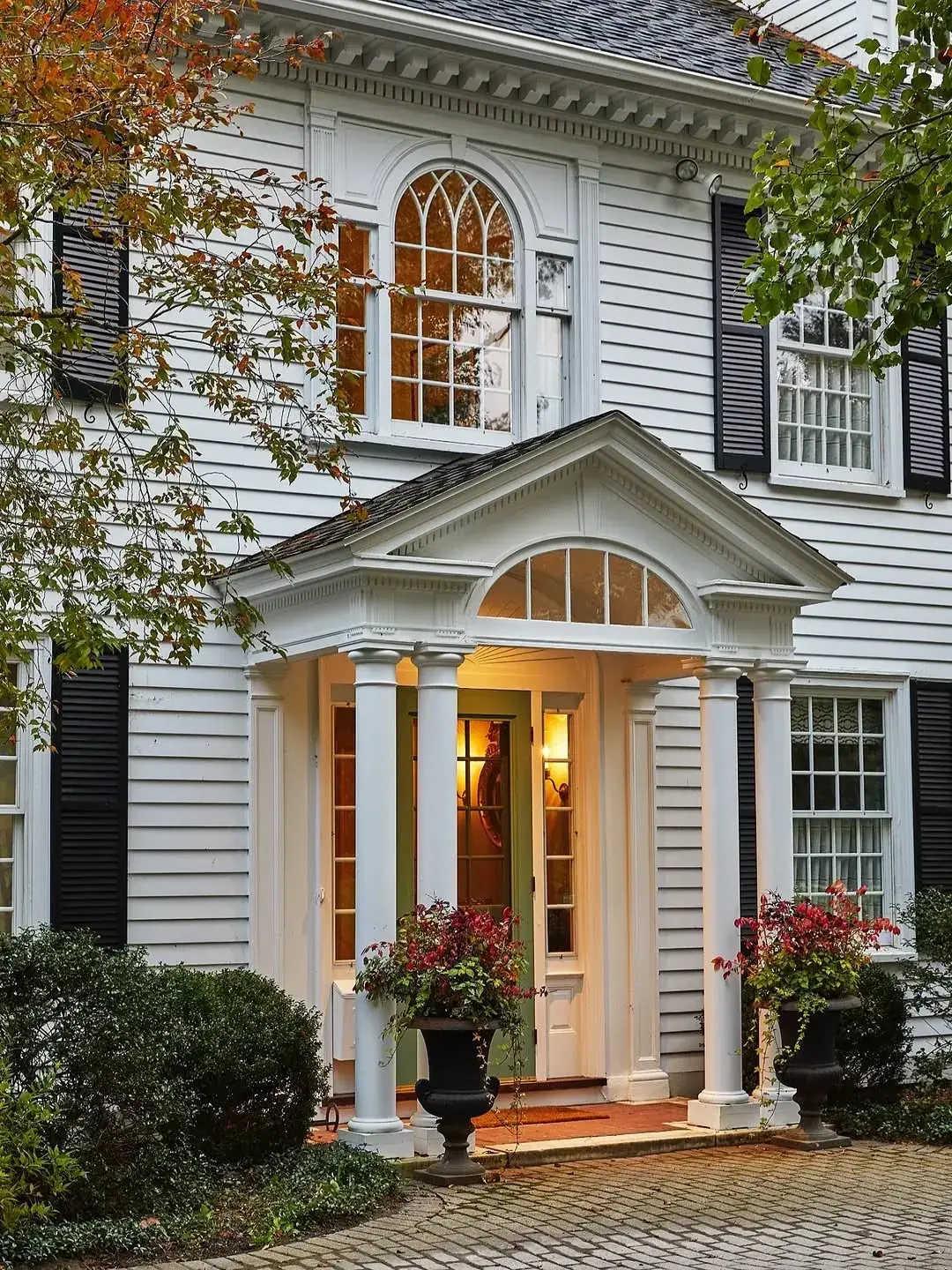 White colonial portico with black shutters, columns and a glowing fanlight over the door