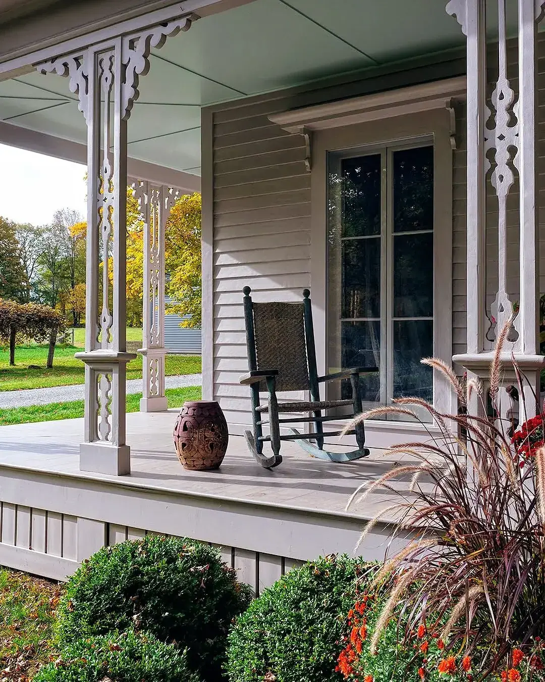 Grey gingerbread porch with fretwork posts and a black rocker with a woven back