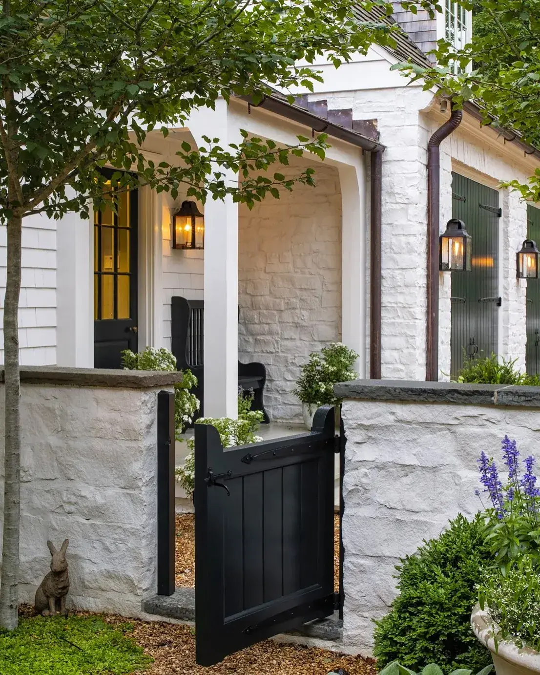 White stone entry with an open black board gate, a black glazed door and bronze lanterns