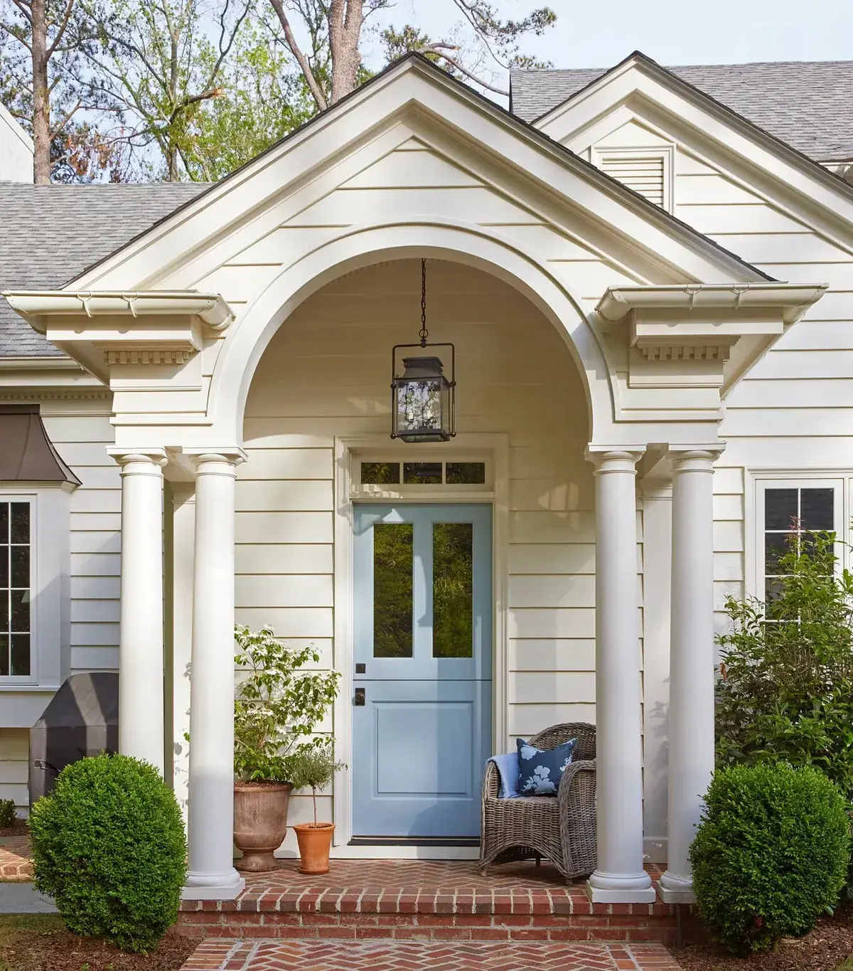 Pale grey-blue Dutch door set deep under an arched portico on a cream clapboard house