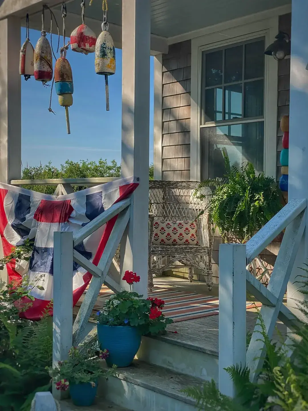 Coastal porch steps with bunting, hanging buoys, wicker chair, and blue plant pots