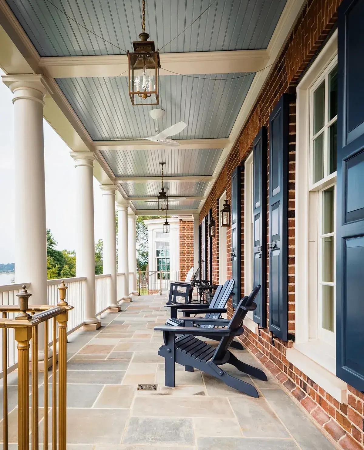 Long brick porch with navy shutters and navy chairs under a pale blue ceiling