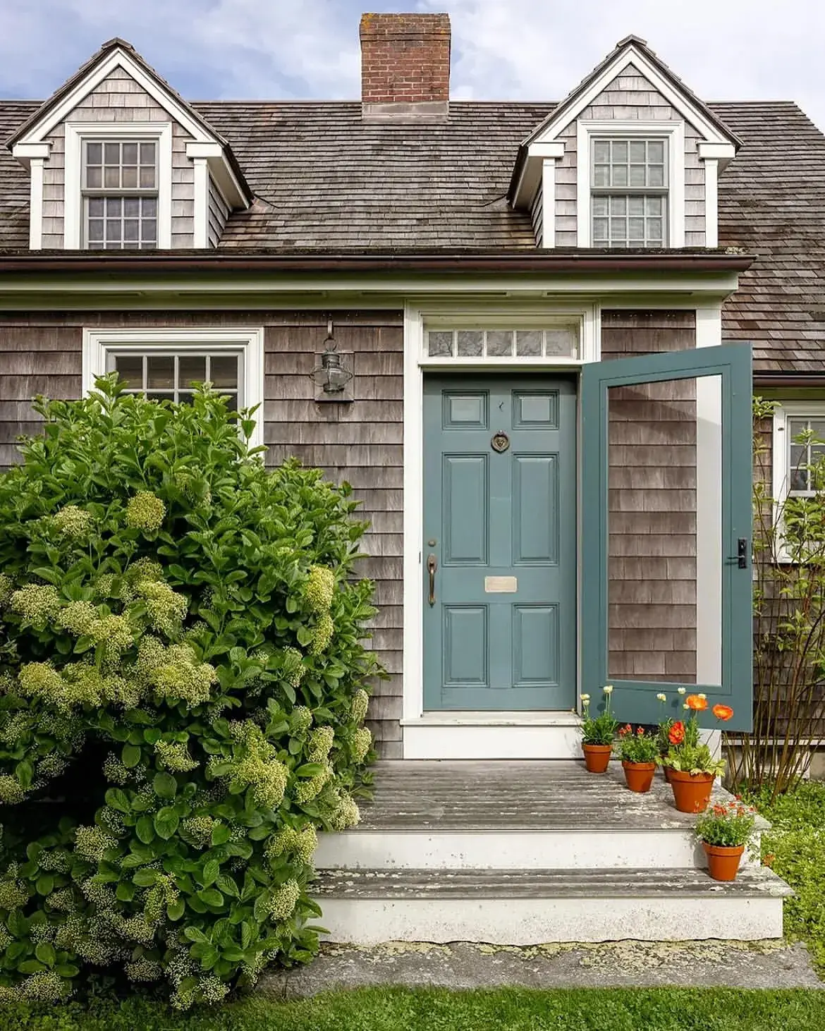 Grey shingle cottage with a dusty teal Dutch door and screen door open