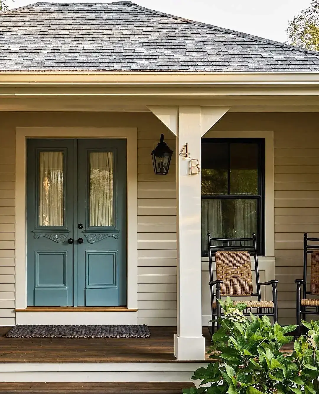 Beige clapboard cottage with dusty blue double doors and rockers