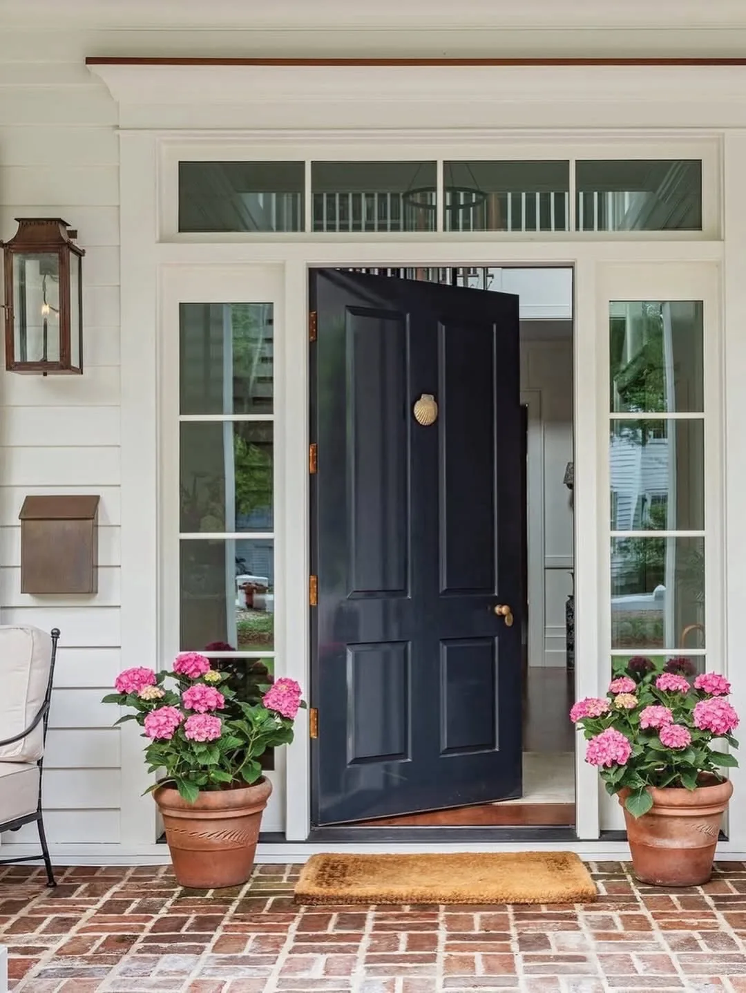 Dark navy door standing open on white clapboard with pink hydrangeas