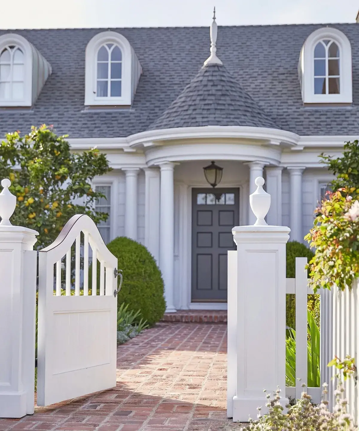 Grey navy door behind white gates with white columns and brick path