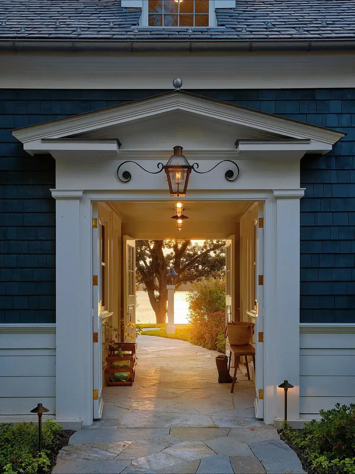 Navy shingle house with white pediment and lantern lit at dusk