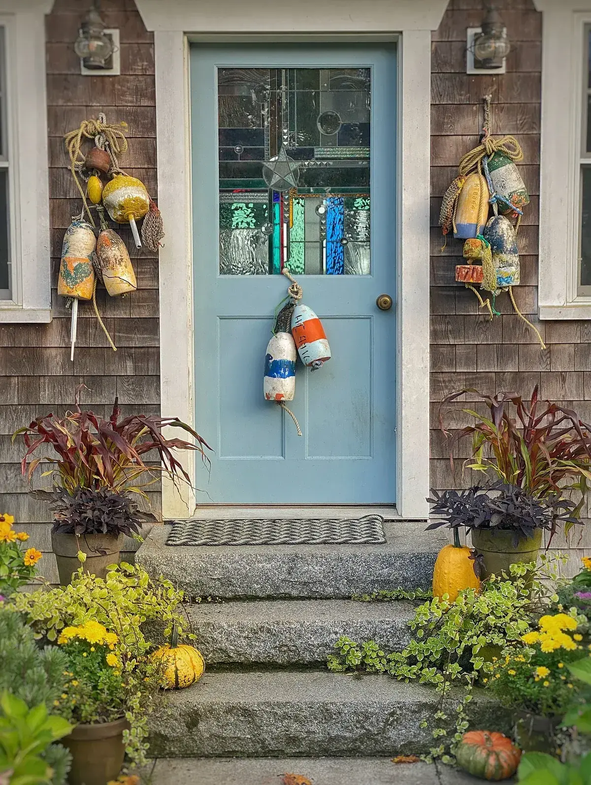 Pale blue door with autumn pots, pumpkins, and buoys on granite steps