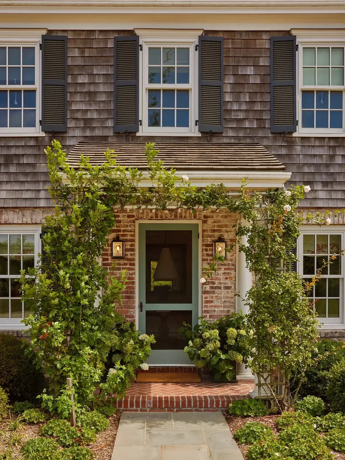 Shingle house with brick door surround, herringbone brick platform and climbing roses