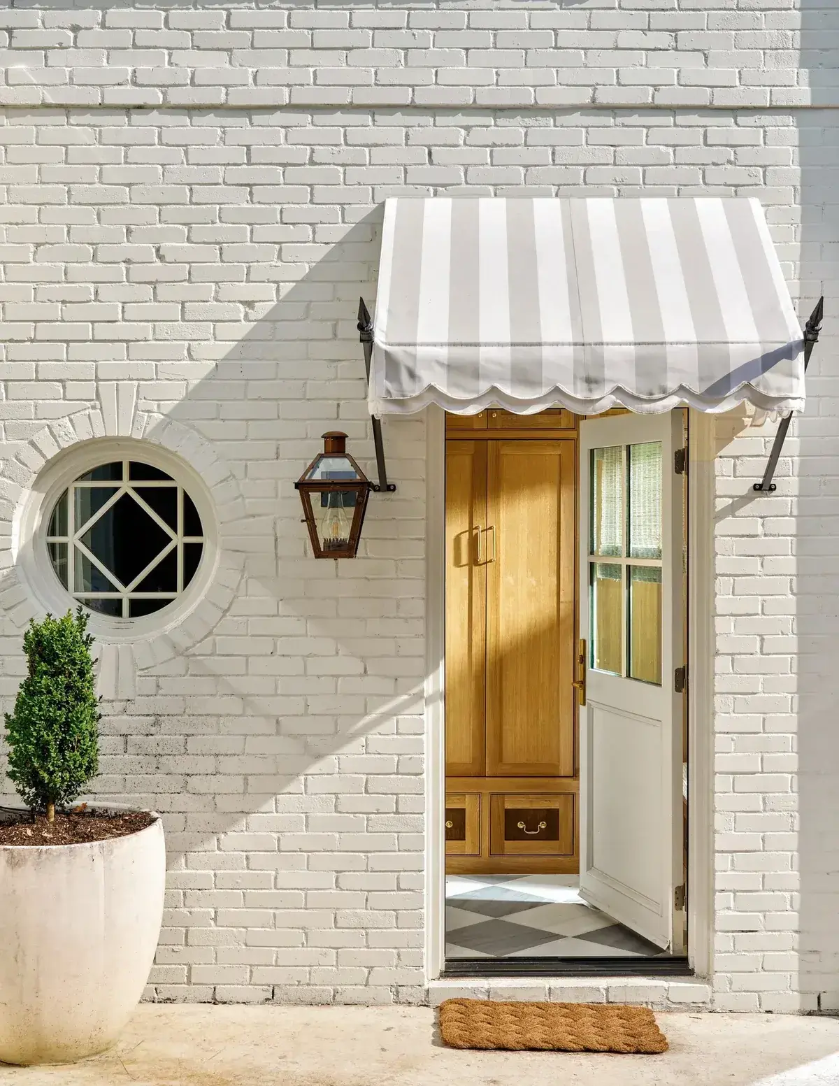 White painted brick wall with striped awning, Dutch door and coir mat