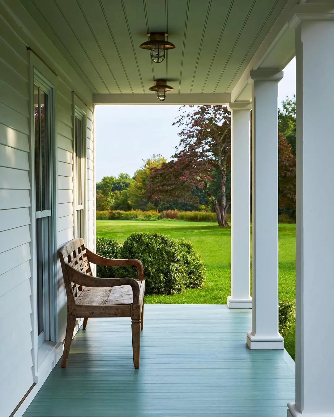 Farmhouse porch with a blue-green painted floor and pale ceiling, holding one weathered chair