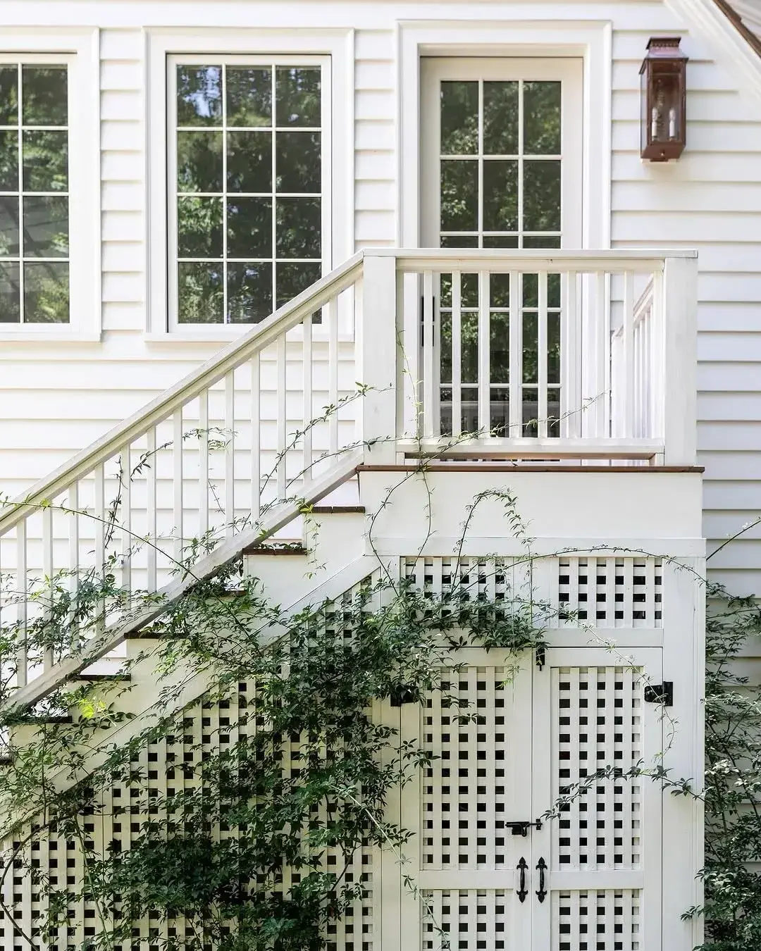 White exterior stairs with open lattice skirting and thin vines growing over the panels