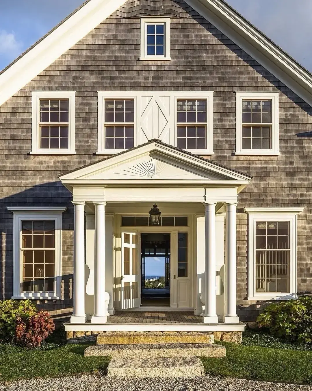 Deep pedimented portico on paired columns against a weathered cedar shingle house