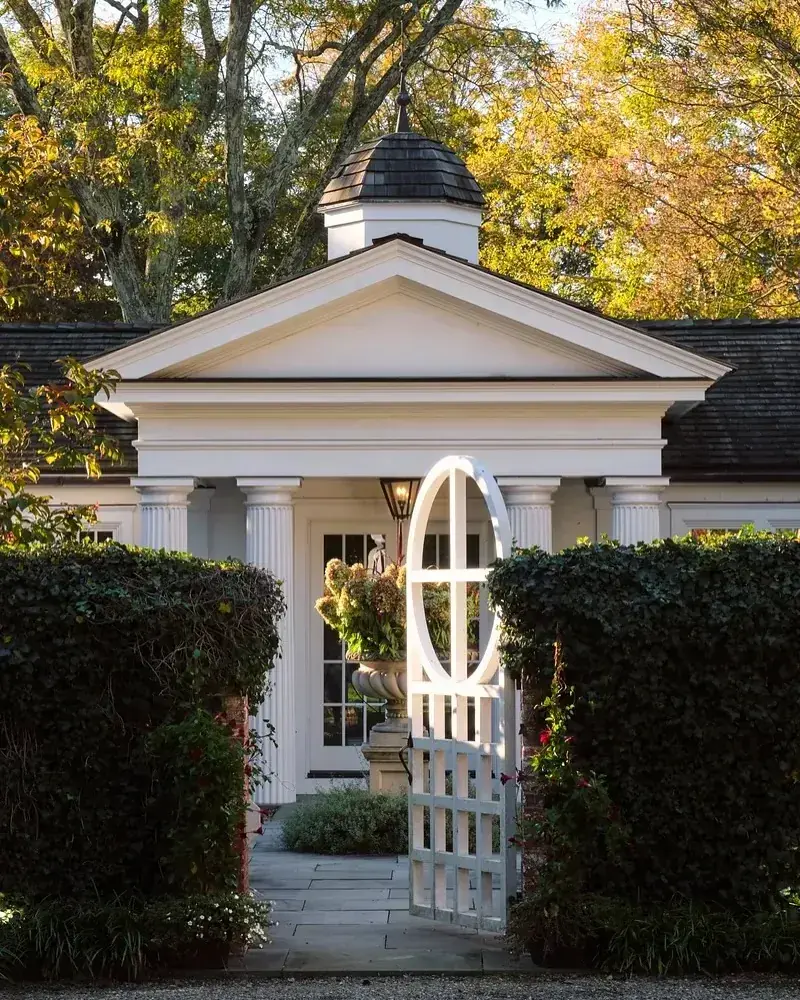 White temple portico with fluted columns, pediment and cupola behind hedges