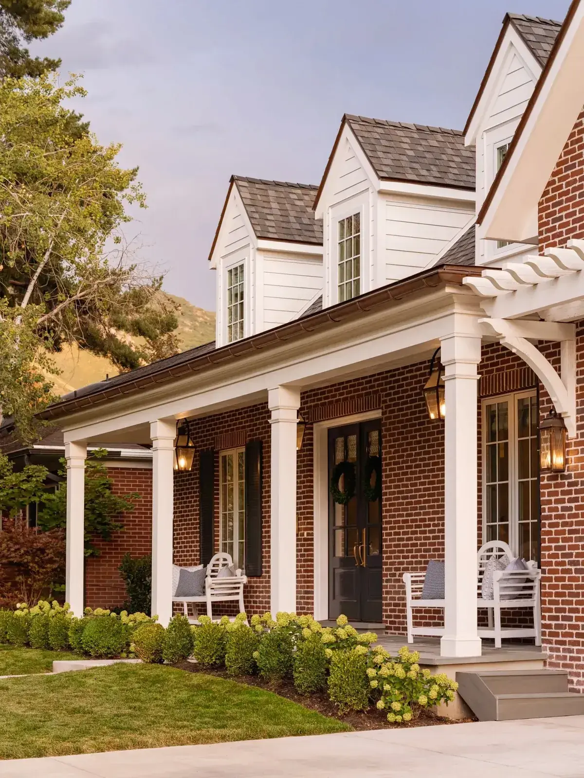 Red brick house with a white columned verandah, dormers and hydrangeas