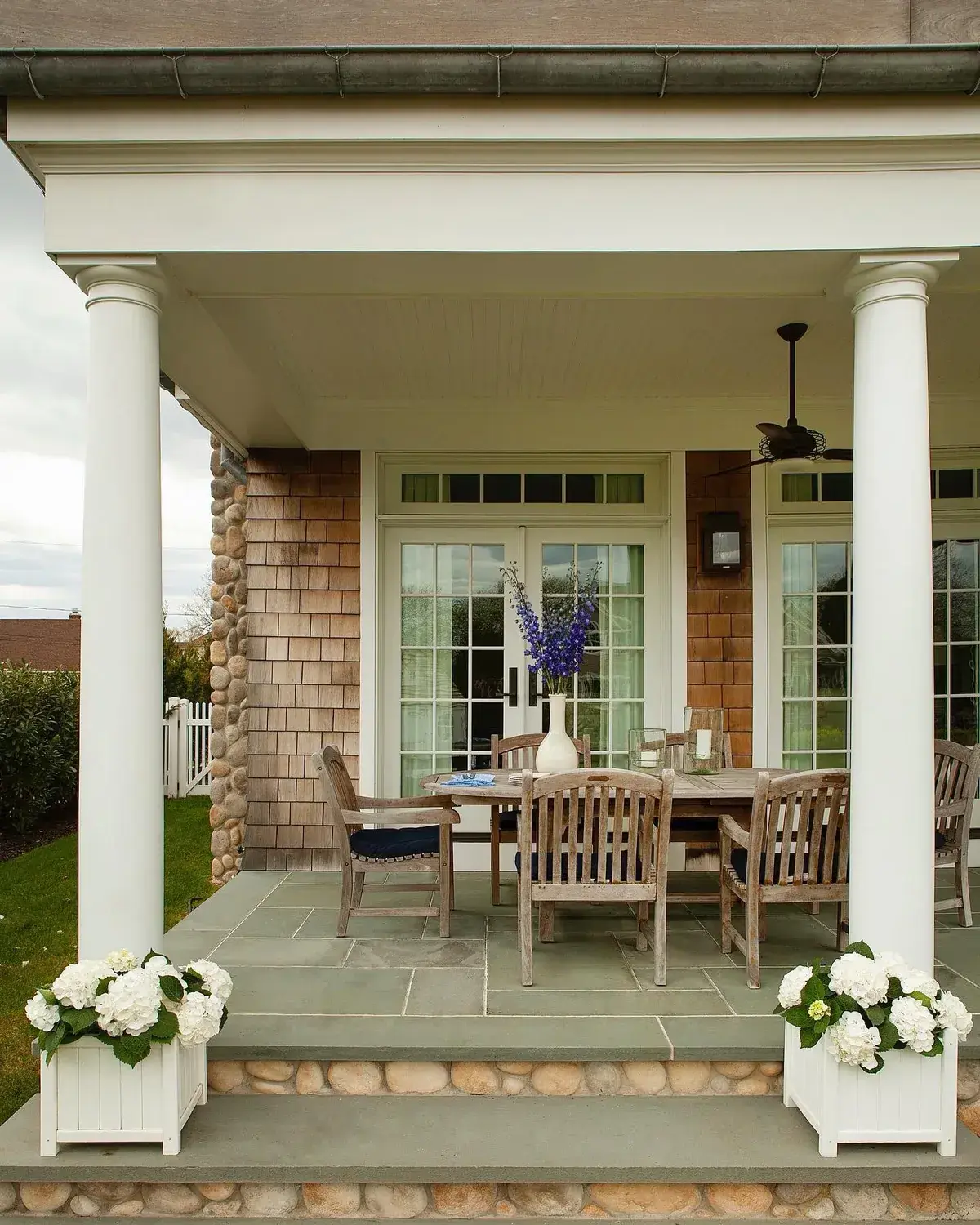 Shingle porch with round columns, stone steps and a teak dining set