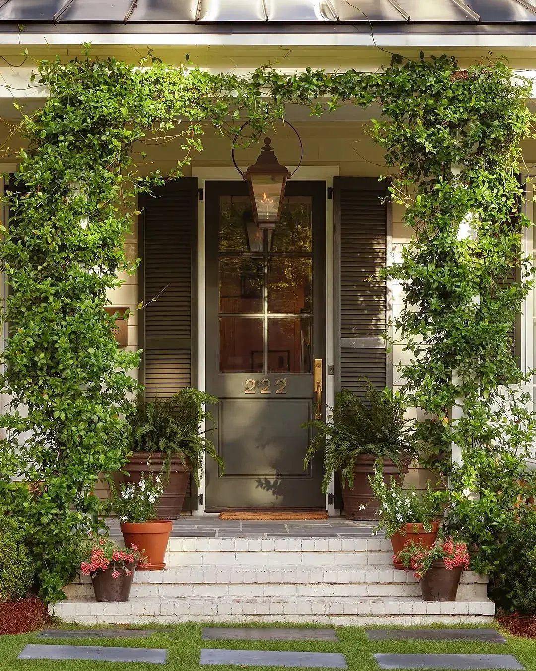 Green door numbered 222 under a vine covered porch with lantern and shutters