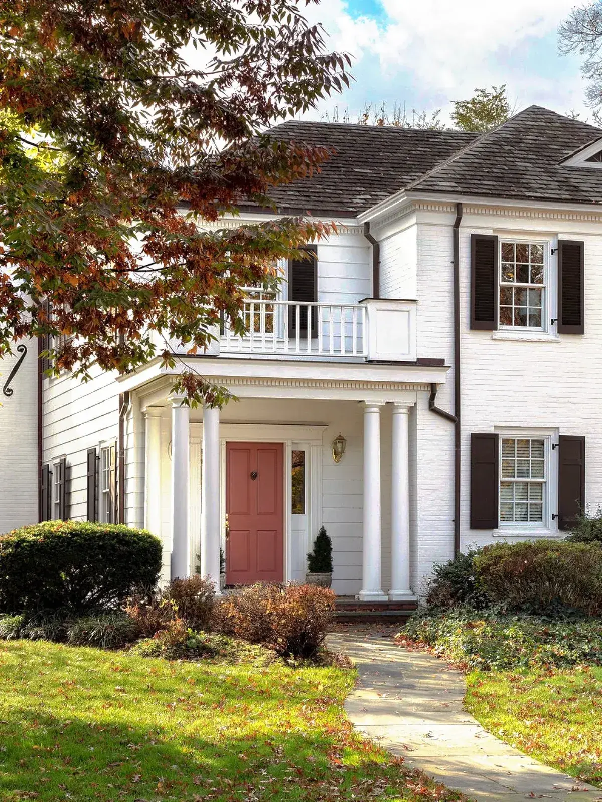 White colonial porch with paired columns, a balcony above and a pink door