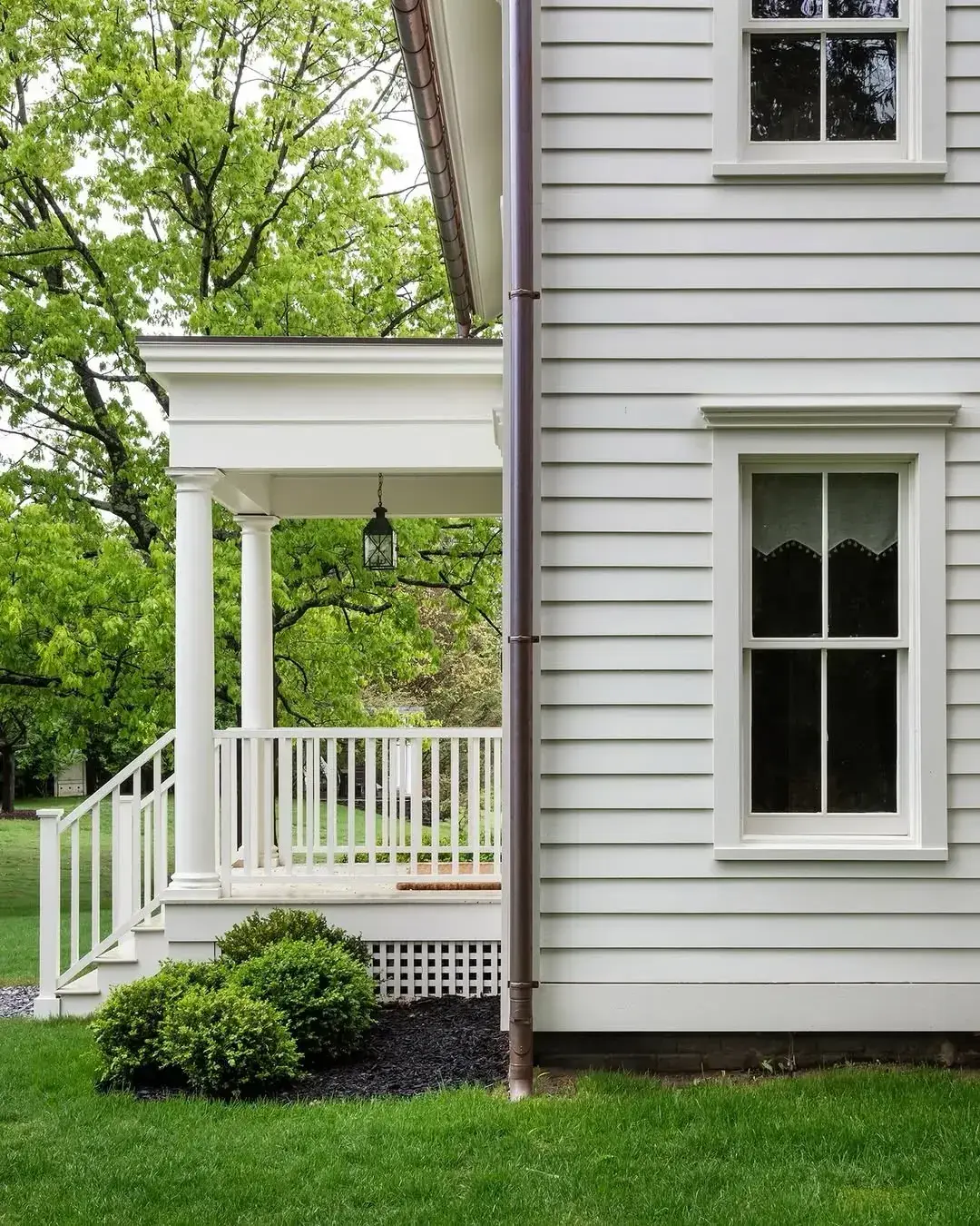 Side of a white porch with columns, railing and lattice skirting