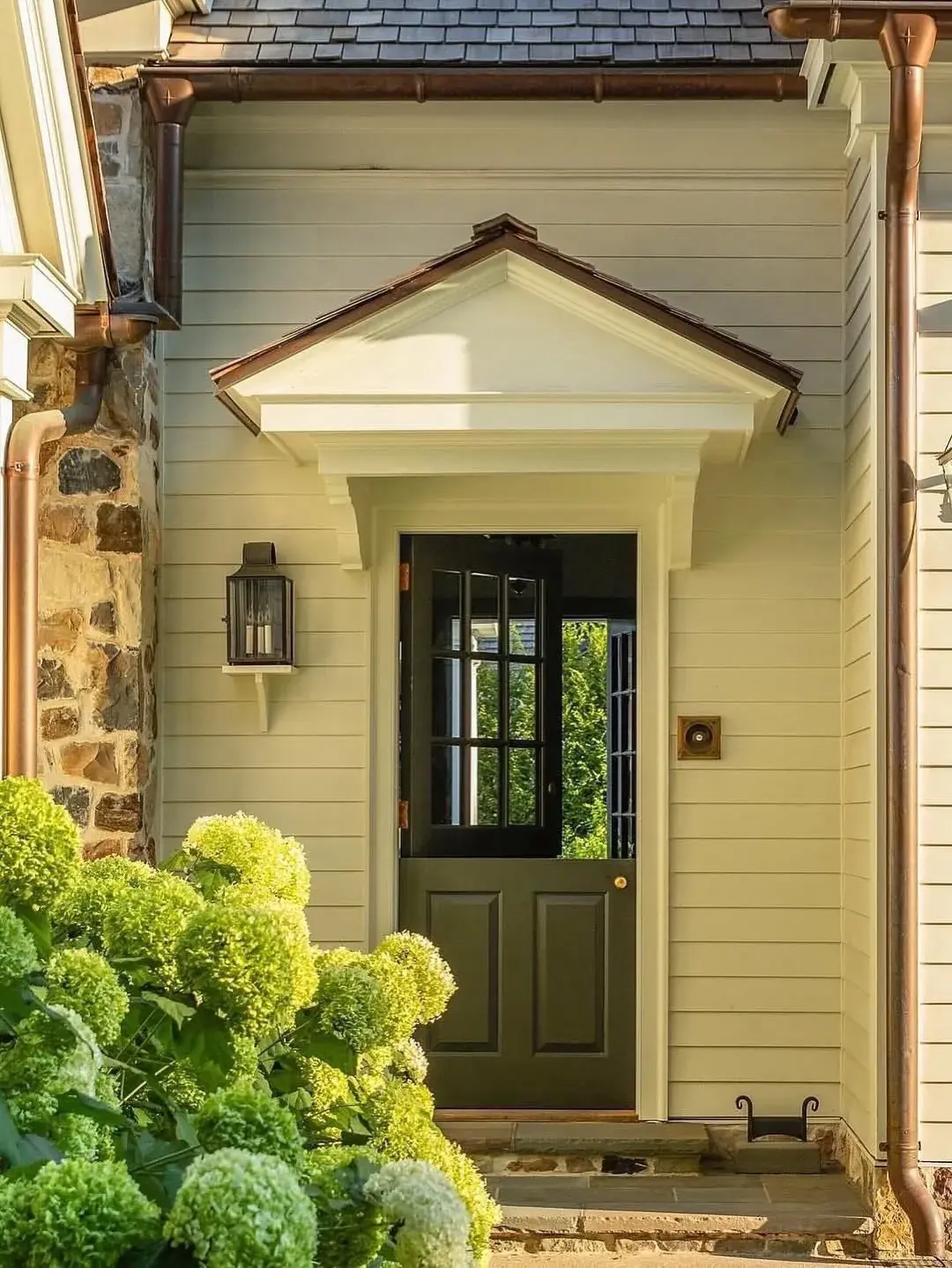 Deep olive green Dutch door under a copper-roofed hood on cream clapboard