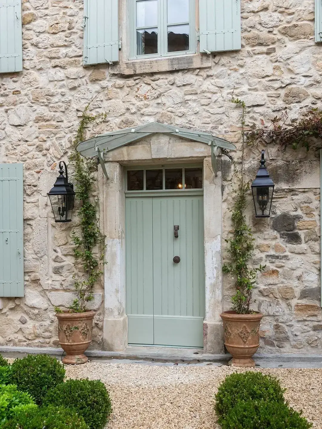 Stone cottage with pale sage double doors and matching shutters under a glass canopy