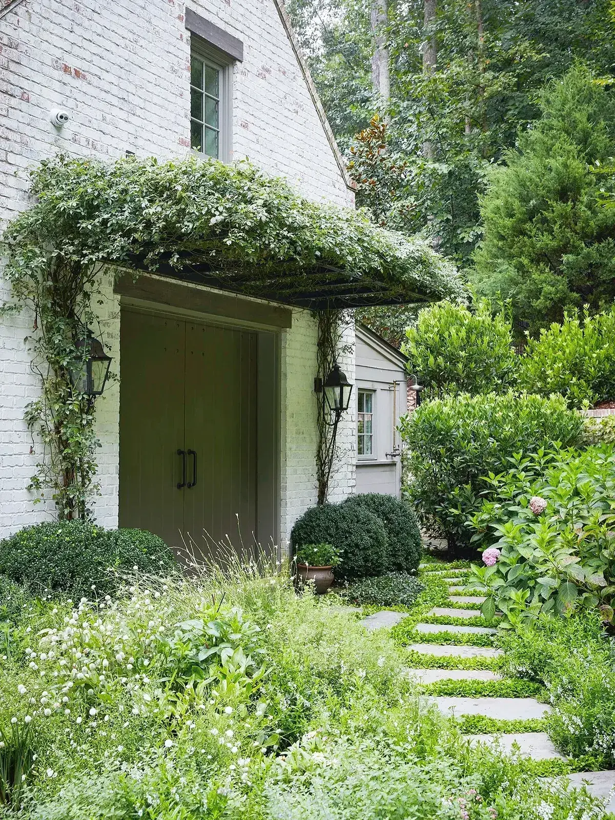 Olive double doors in whitewashed brick under a vine covered pergola