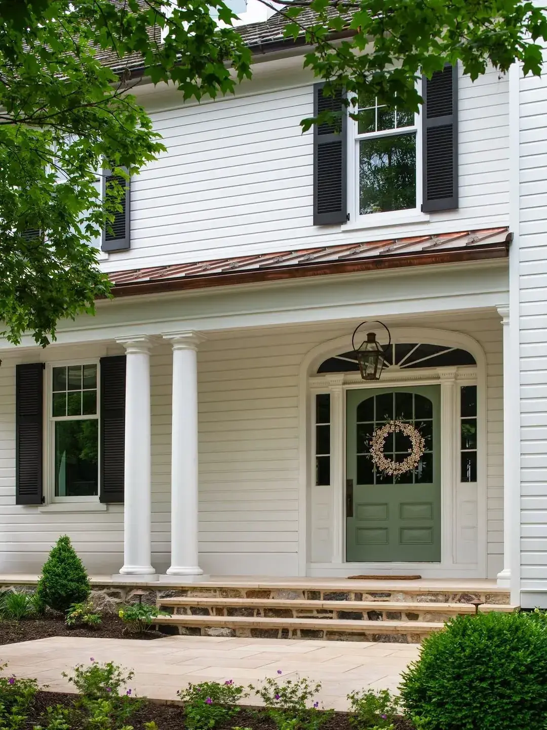 Sage green glazed door with wreath on white clapboard house with copper porch roof