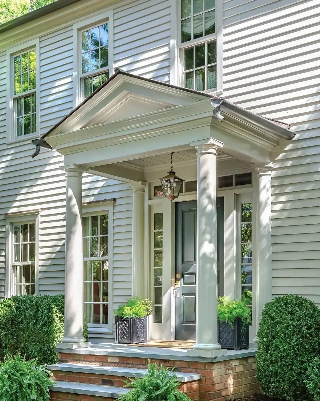 Dark green door set deep in a columned portico on grey clapboard