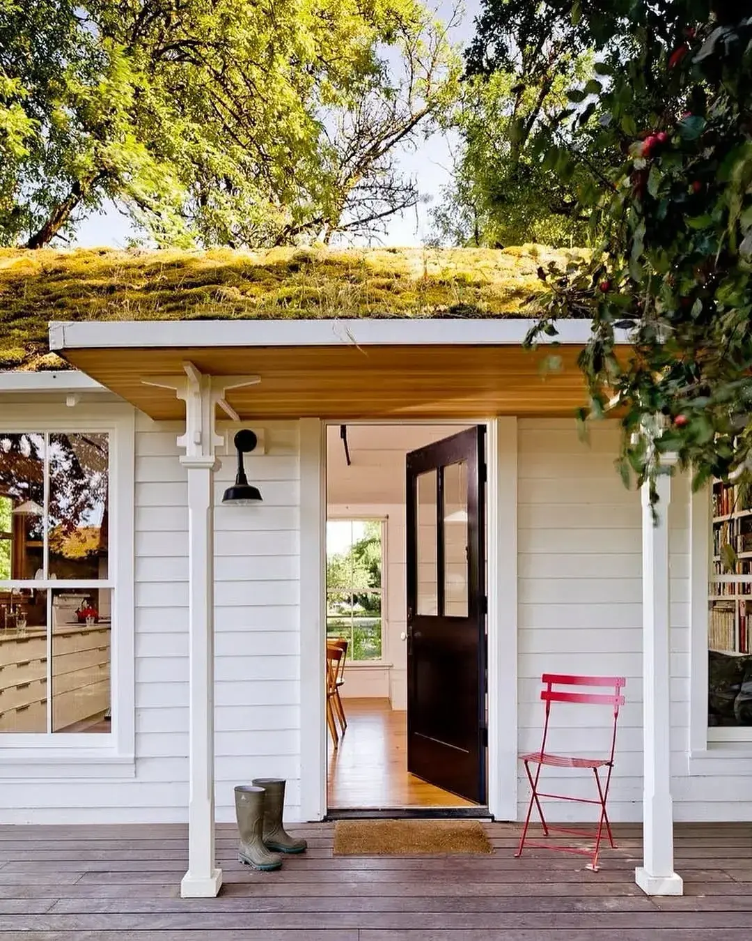 Near-black green door standing open on white cottage with living turf roof
