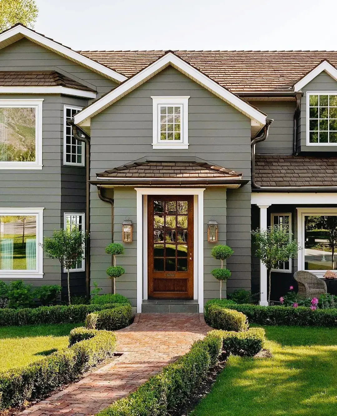 Grey clapboard front with a glazed timber door, clipped standards, and low hedging along a brick path