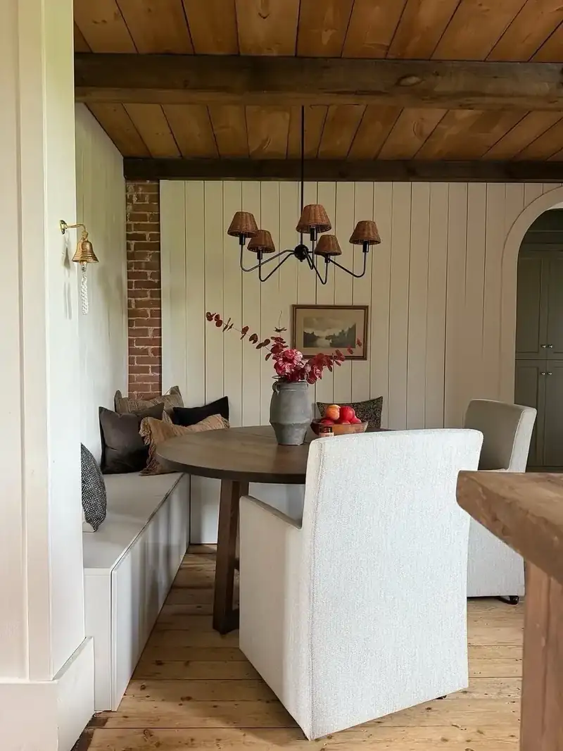 Built-in white banquette with grey and patterned cushions beside an oval pedestal table and slipcovered chairs