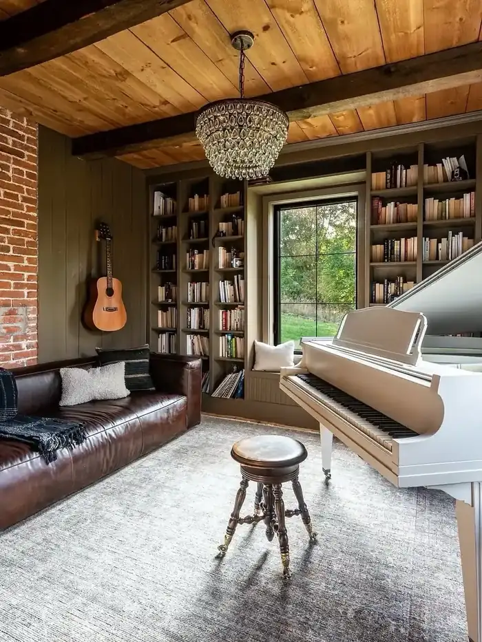 Music room with a white grand piano, aged leather sofa, olive panelled walls and full bookshelves