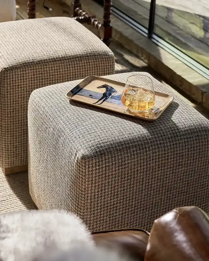 Two woven ottomans used as a coffee table with a printed metal tray and a glass