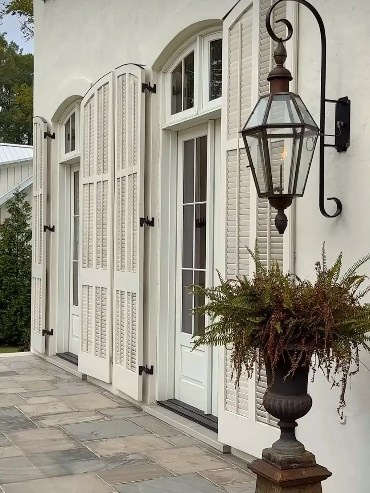 White stucco house with tall white arched louvered shutters, pintle hinges and a large copper lantern