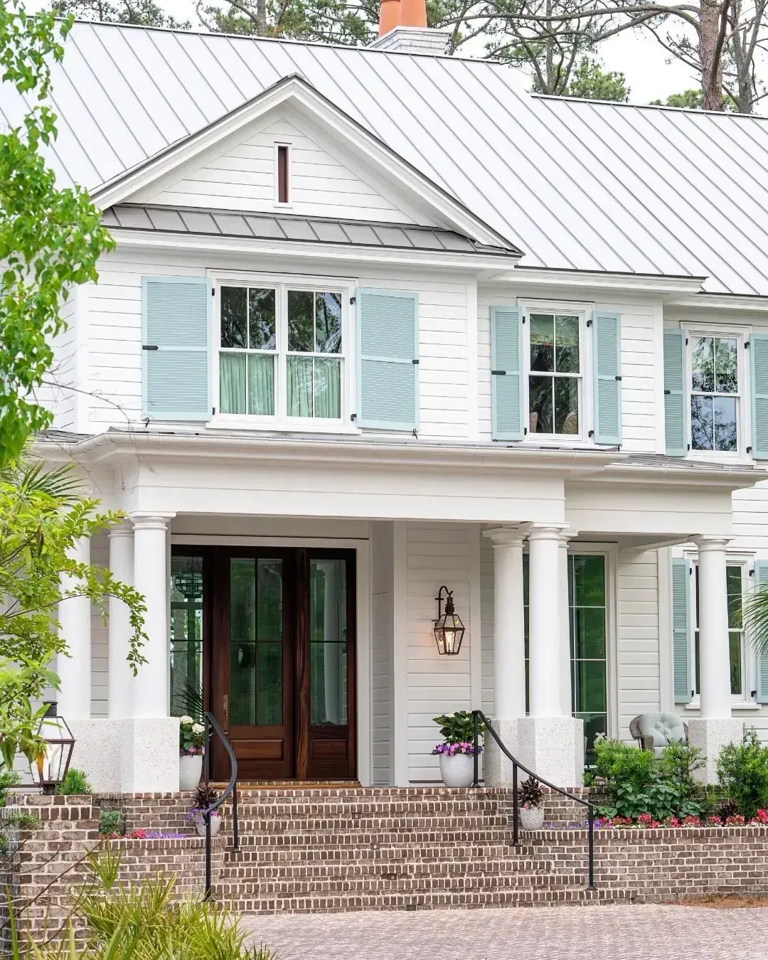 White house with pale aqua louvered shutters, standing seam metal roof and brick steps