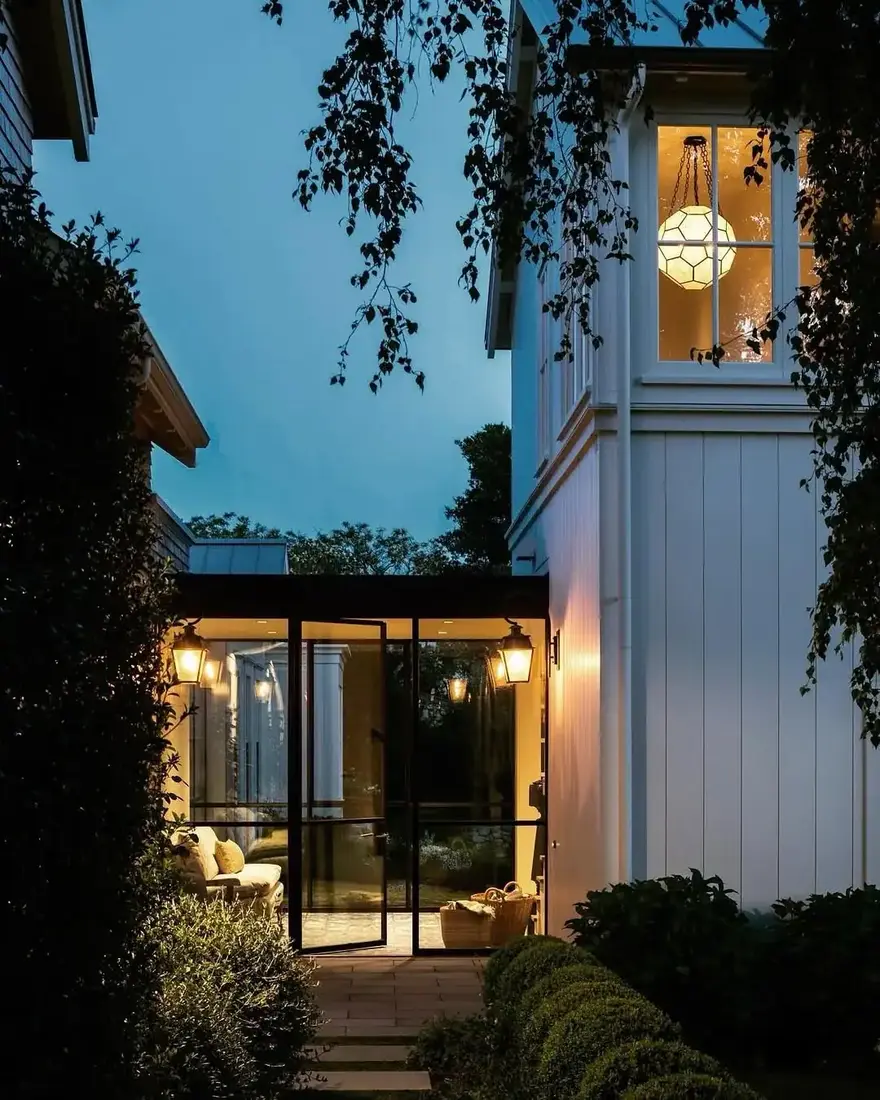 White vertical boarded house joined by a glass link glowing at dusk