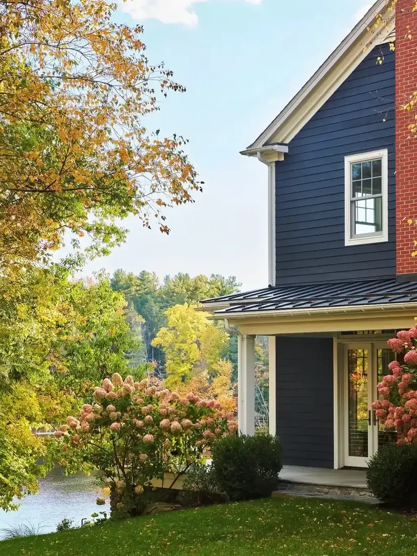 Dark navy house with horizontal cladding beside a lake with hydrangeas