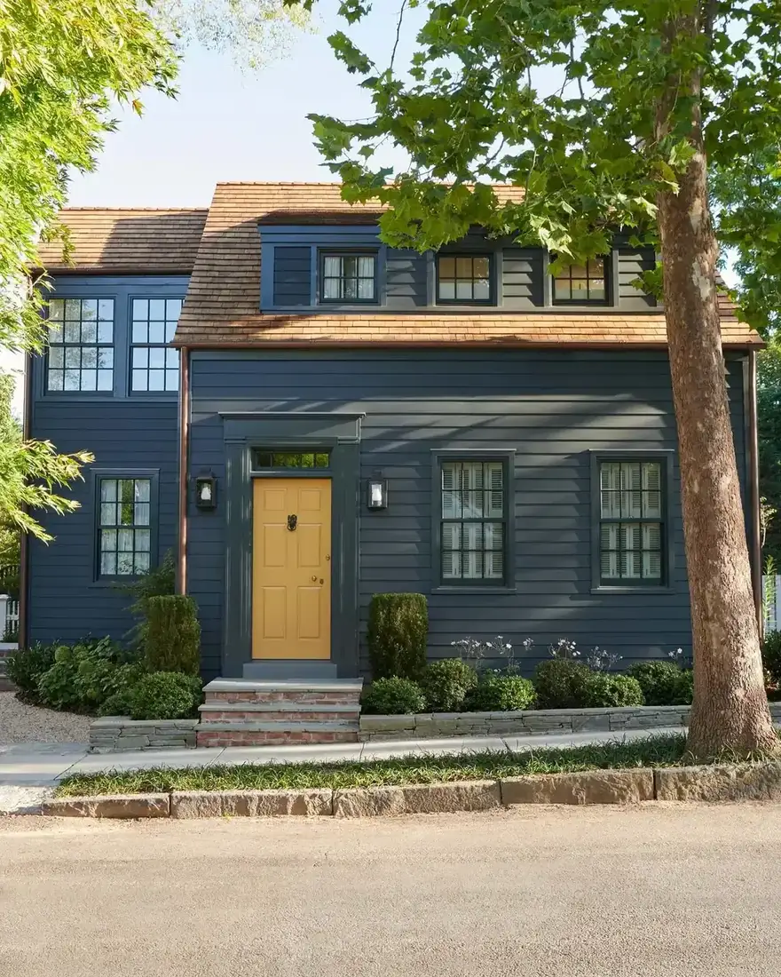 Dark navy clapboard house with a mustard yellow front door and shingle roof