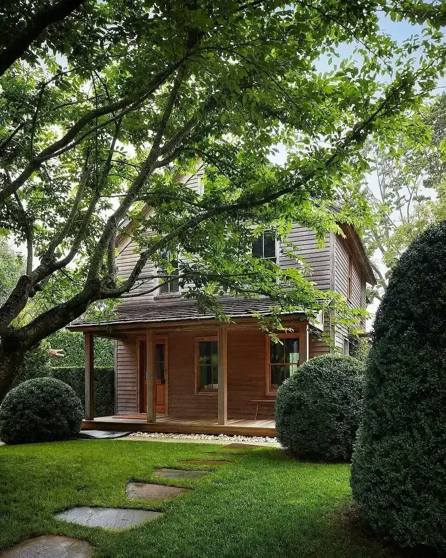 Weathered timber cottage with horizontal boards, small porch and oak tree
