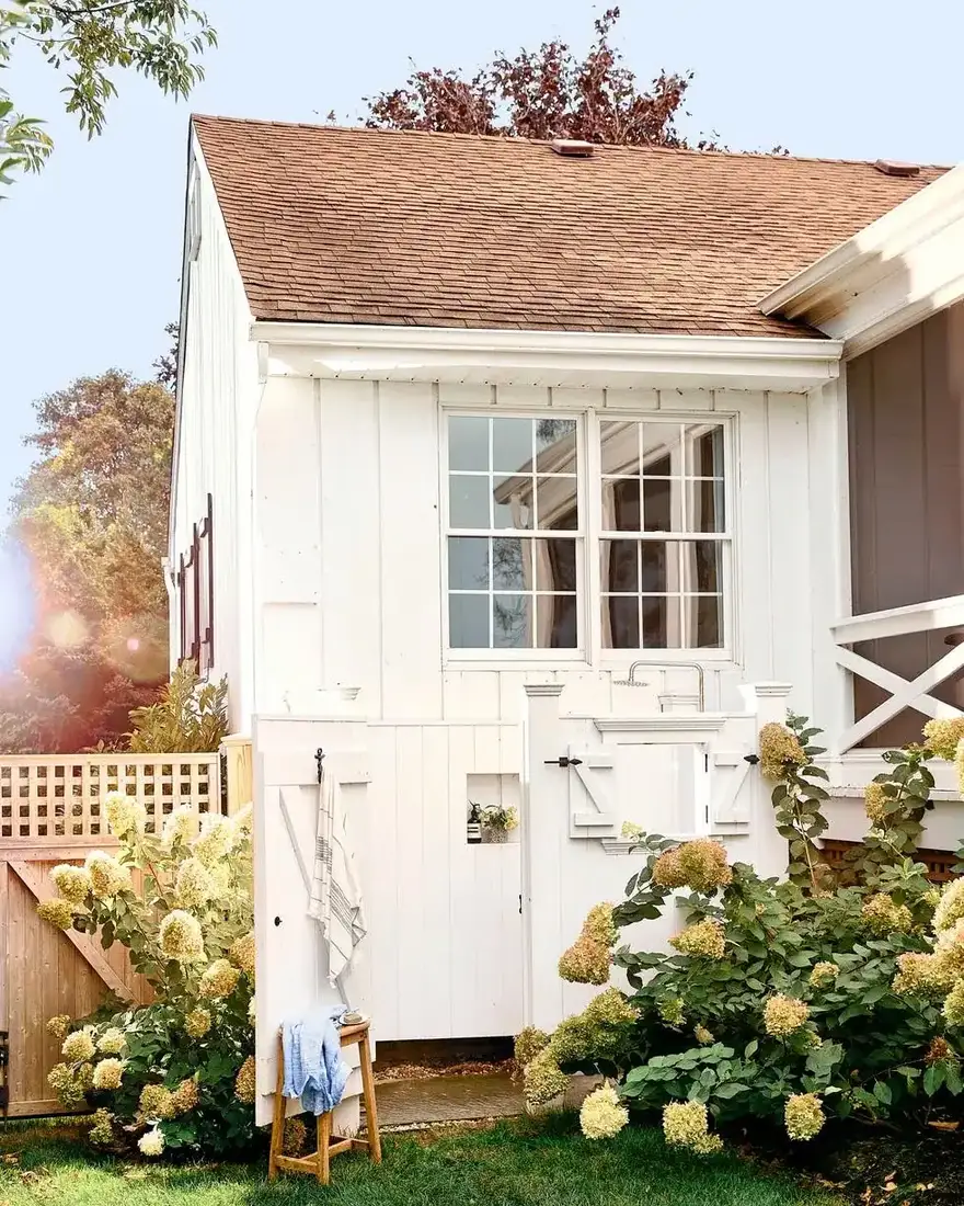 Small white outbuilding with vertical boarding, open side doors and hydrangeas beside it