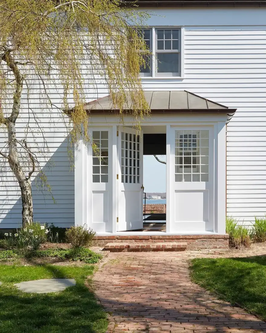 White clapboard house with a small glazed entry porch, copper roof and brick path